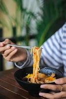 eating spaghetti hand gesture in black bowl with chopsticks on wooden table photo