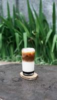 Iced coffee with milk in a glass on wooden table and green grass background photo