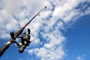 Spinning fishing rod against blue sky and clouds. Sport fishing, hobby, leisure and vacation photo