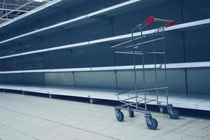 Shopping trolley in front of empty shelves in grocery store photo