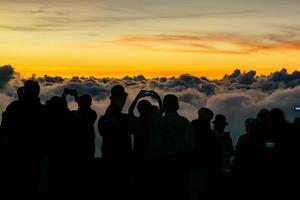 Silhouette person group watching floating sea of clouds,Sea of fog, Sky above clouds,taking cloudscape photos with mobile phones in the morning,sun rising,travel long weekend,Inthanon mountain.