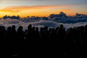 Silhouette person group watching floating sea of clouds,Sea of fog, Sky above clouds,taking cloudscape photos with mobile phones in the morning,sun rising,travel long weekend,Inthanon mountain.