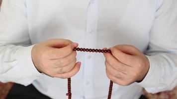 musulmán hombre en un blanco camisa adorando rosario en su mano, uno de el accesorios usado para Adoración después oración es el rosario video