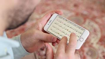 une Jeune homme zoome dans et regards à le coran pages de le écran de le téléphone il est holding, le image de une musulman ouverture le coran de une téléphone intelligent dans le masjid video