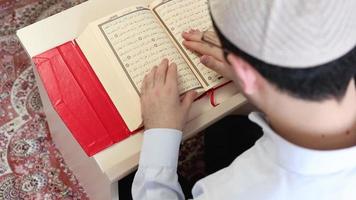 een moslim Mens in een religieus hoed lezing de Pagina's van de koran staand Bij de tafel, verduidelijkt beeld van de koran video