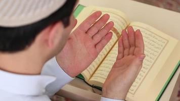 el Corán y un Orando hombre en pie a el mesa, un musulmán adolescente frota su manos en su cara después Orando a Alá video