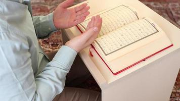 imagen de un abierto Corán y Orando del hombre manos en el mesa, musulmanes leer su religioso libros y orar a Alá video