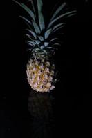 Pineapple fruit isolated on black background with reflection in its shadow. photo