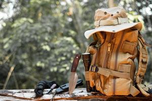 Equipment for survival bucket hat backpack hiking knife camping flashlight resting on wooden timber in the background is a forest photo