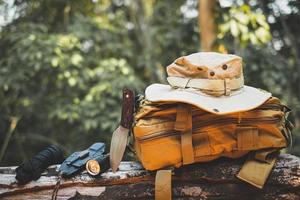 Equipment for survival bucket hat backpack hiking knife camping flashlight resting on wooden timber in the background is a forest photo