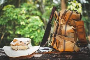 Equipment for survival bucket hat backpack hiking knife camping flashlight resting on wooden timber in the background is a forest photo