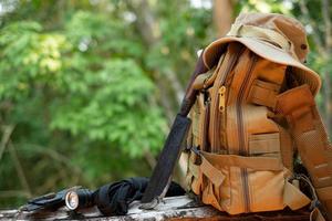 Equipment for survival bucket hat backpack hiking knife camping flashlight resting on wooden timber in the background is a forest photo