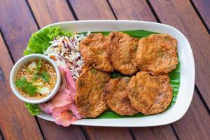 Top view. Fried fish paste balls or deep fried fish cake Contains curry paste as ingredient It is spicy Thai dish served with dipping sauce mixed with cucumber. Asian food style. photo