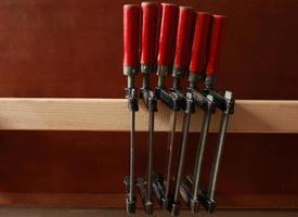 row of clamps with red handles hang on a shelf in a carpentry workshop photo