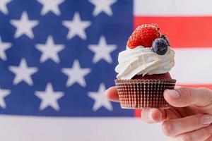 hand holding sweet cupcake with blueberries and strawberry , flag background photo