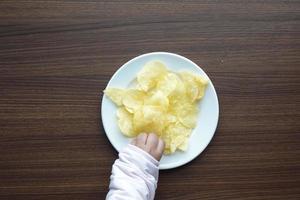 child hand reaching for potato chips on a plate photo
