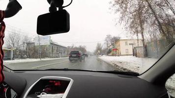 NOVOSIBIRSK, RUSSIA OCTOBER 31, 2021 - Snow falling on city street. POV inside car in drive through wet windshield video
