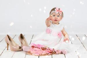 One year old child with a birthday cake. Funny little girl smeared with cream on the first anniversary. Funny child on holiday. photo