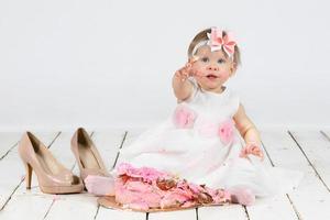 One year old child with a birthday cake. Funny little girl smeared with cream on the first anniversary. Funny child on holiday. photo