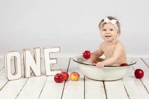 A happy child bathes in a basin. Beautiful little girl in one year. Little one with letters. photo
