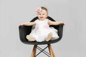 The child is one year old. Beautiful little girl is sitting on a chair. Funny child with a bow. Charging baby. photo