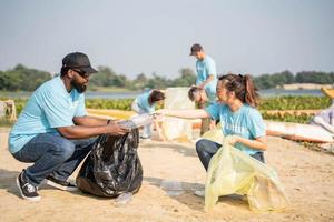 volunteering, charity, cleaning, people and ecology concept - group of happy volunteers with garbage bags cleaning area on sandy shore. photo