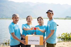 Happy Team of volunteers holding red heart, showing object at camera, smiling. Team promoting charity, donation campaign, health insurance, medical checkup. photo