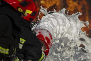 Firefighter puts out a fire. Silhouettes of firefighters with hoses with foam on a background of fire. photo