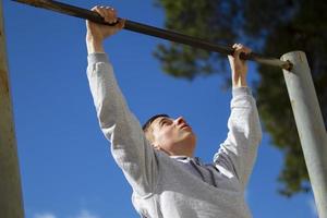 The boy pulls himself up on the horizontal bar on the street. A young man does exercises. photo