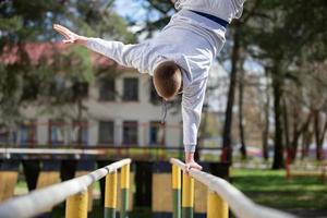 un hombre lo hace ejercicios en desigual barras en el calle. un hombre va en para Deportes. foto