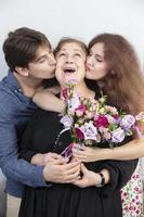 Holiday at the woman. Elderly woman with a bouquet of flowers surrounded by children. Boyfriend and girlfriend kiss grandmother. Children congratulate mom. Happy adult woman accepts congratulations. photo