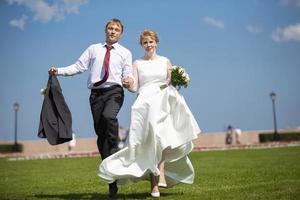 Bride and groom. Beautiful newlyweds run on the grass against the sky. photo