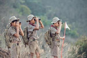 American Boy Scouts in uniform sit binoculars in a green field on a mountain hike going to summer camp. photo