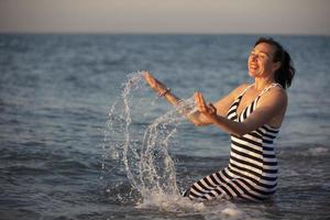 descanso a el complejo. mayor mujer en vacaciones por el mar con rociar de agua.curación mar agua. foto