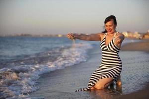 Happy woman on vacation at sea. Woman pours sand on the beach. photo