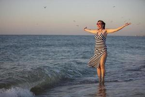 Happy middle aged woman by the sea with hands up. photo