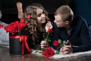 Beautiful young couple at home. Hugs, kisses and enjoys spending time together, celebrating Valentine's Day with red roses. photo