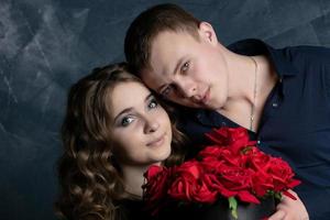 Portrait of a beautiful couple in love on a dark background. Faces of a girl and a guy close-up with roses. Valentine's Day. photo