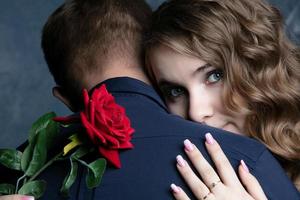 The face of a beautiful girl with a red rose on the shoulder of a guy. Valentine's Day. Lovers. Romantic date. photo