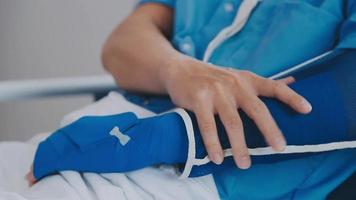 Mens met gebroken arm in gips aan het liegen Aan bed in ziekenhuis. de noodgeval centrum behandeling is gips en blijft hangen met draagdoek voor een verder genezen in een orthopedische kliniek. geduldig pijn van ongeluk blessure. video