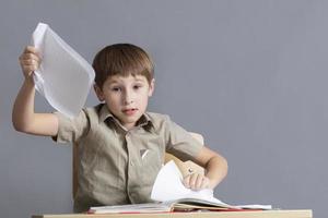 el niño es enojado a tarea. un elemental colegio estudiante es desgarro papel. foto