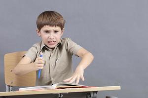 A primary school student is doing homework. The child at the desk with the textbook is angry. The boy does not want to study. A seven-year-old child goes crazy for lessons. photo