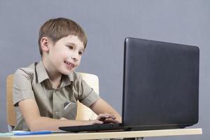 el niño a el ordenador portátil. el chico mira a el monitor pantalla. preescolar a el computadora. júnior estudiante a un mesa con un computadora. foto