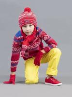 A child in warm clothes. A boy in a red hat and sweater and sneakers. Fashionable boy in the studio. photo