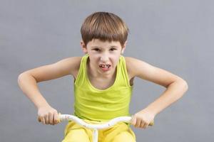 niño en un bicicleta en un gris antecedentes. gracioso pequeño chico obras de teatro un motociclista. foto