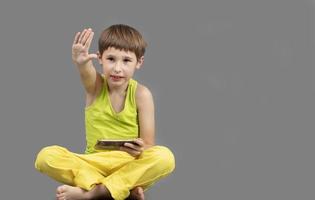 Child on a gray background with a mobile phone with a raised hand. photo