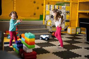 Two sisters playing at kids play center while build with colored plastic blocks. photo