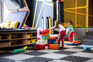 Two sisters playing at kids play center while build with colored plastic blocks. photo