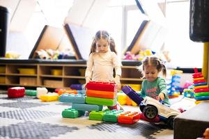 Two sisters playing at kids play center while build with colored plastic blocks. photo