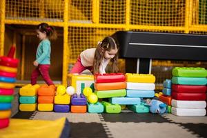 Two sisters playing at kids play center while build with colored plastic blocks. photo